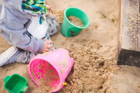 Quelle: pixabay.com / kaboompics, https://pixabay.com/de/photos/sandkasten-kind-spielzeuge-eimer-762541/ Kind spielt mit Eimern im Sandkasten